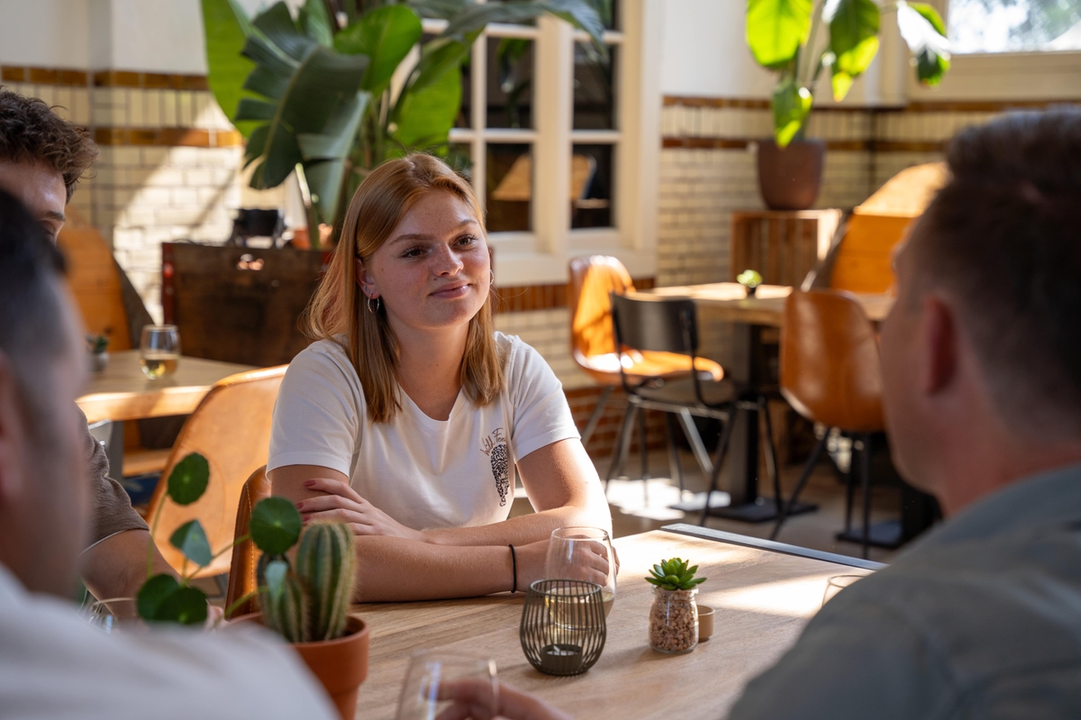 Groep mensen in gesprek aan een tafel in een lichte ruimte.