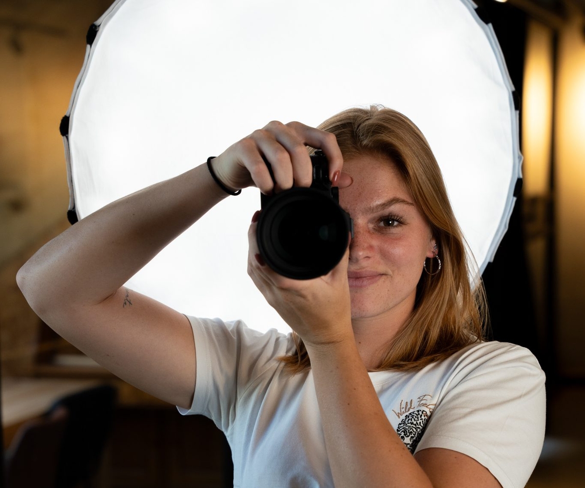 Fotograaf richt camera naar voren met softbox op de achtergrond.