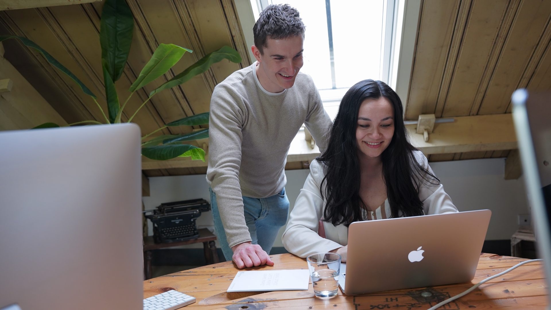 Man en vrouw werken samen achter een MacBook in een licht kantoor.