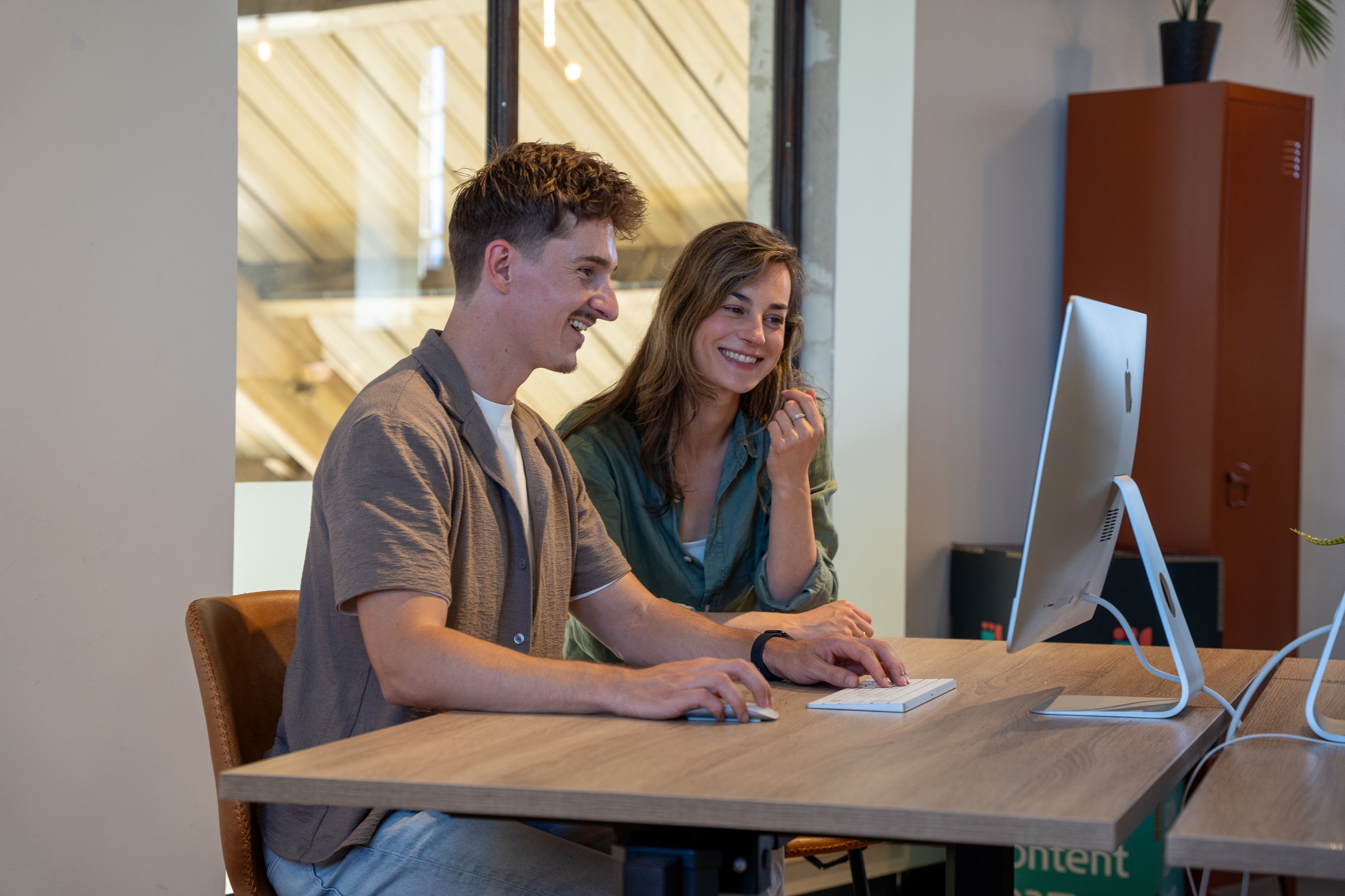 Jordi en Iris zitten samen lachend achter een computer aan een bureau.