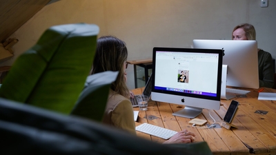 Twee vrouwen werken achter iMacs aan een houten tafel in een creatief kantoor.