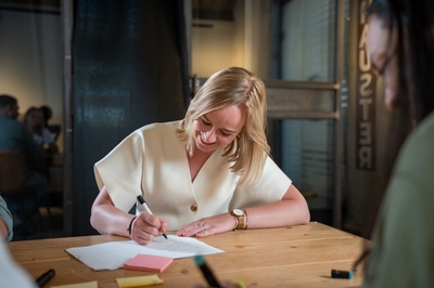 Vrouw schrijft lachend aantekeningen tijdens een creatieve sessie.