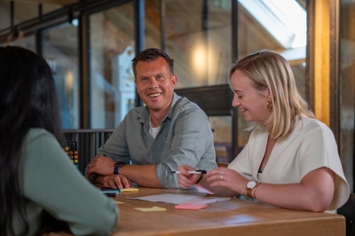 Thomas en Dorinke zitten aan tafel in gesprek, met papieren en notities voor zich.