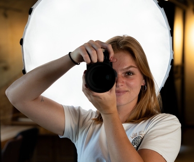 Fotograaf richt camera naar voren met softbox op de achtergrond.