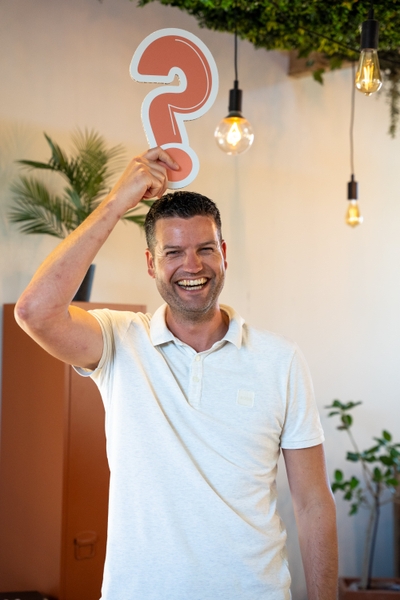 Lachende man houdt rood vraagteken boven zijn hoofd.