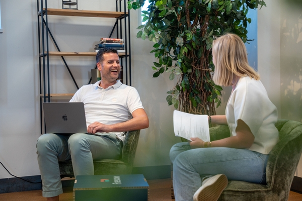 Twee collega’s in gesprek, één met laptop en één met papieren.