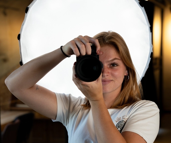 Fotograaf richt camera naar voren met softbox op de achtergrond.
